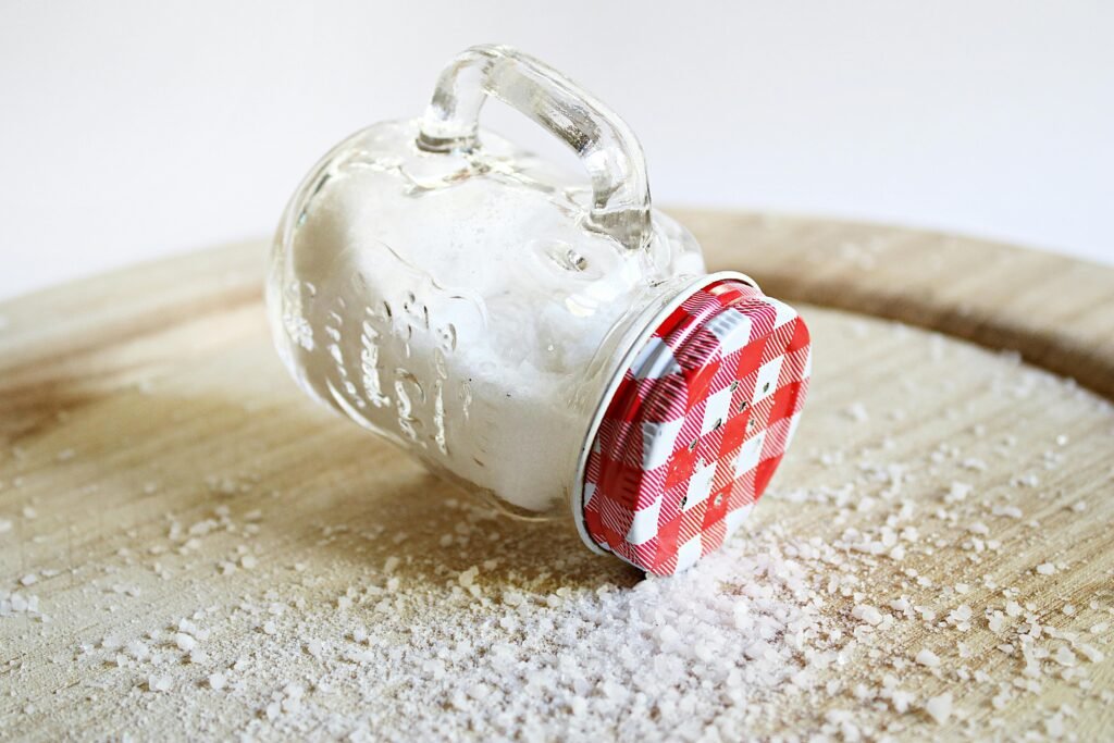 Overturned mason jar with red lid spilling salt on a wooden surface, creating a rustic kitchen scene.