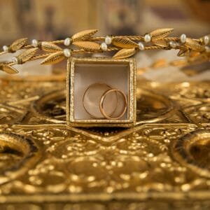 Close-up of gold wedding rings and a delicate tiara on an ornate golden background, symbolizing luxury and elegance.