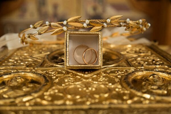 Primer plano de unas alianzas de oro y una delicada tiara sobre un fondo dorado ornamentado, símbolo de lujo y elegancia.