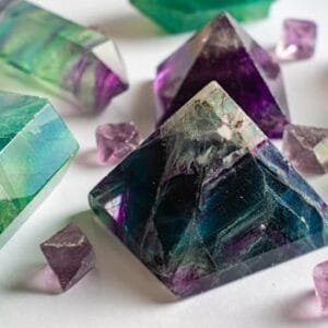 Close-up of colorful fluorite and amethyst crystals in various shapes on a white surface.