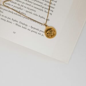 A close-up view of a gold pendant necklace resting on an open book with white pages and text.