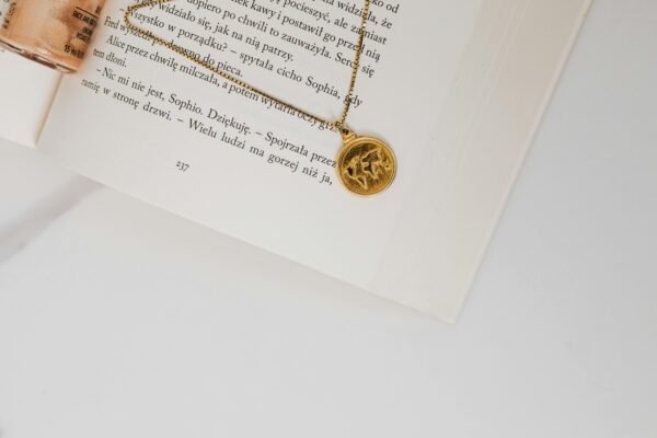 A close-up view of a gold pendant necklace resting on an open book with white pages and text.